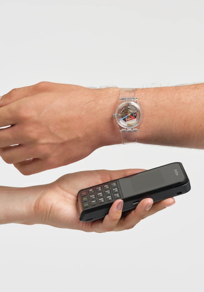 A hand with an analog watch, approaching a mobile phone