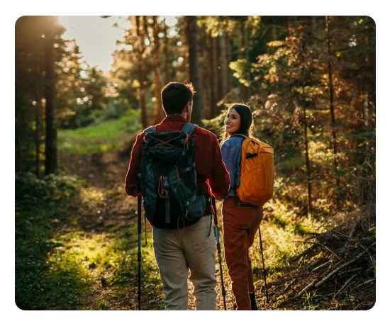Homem e mulher caminham na floresta, ela olha para trás a sorrir