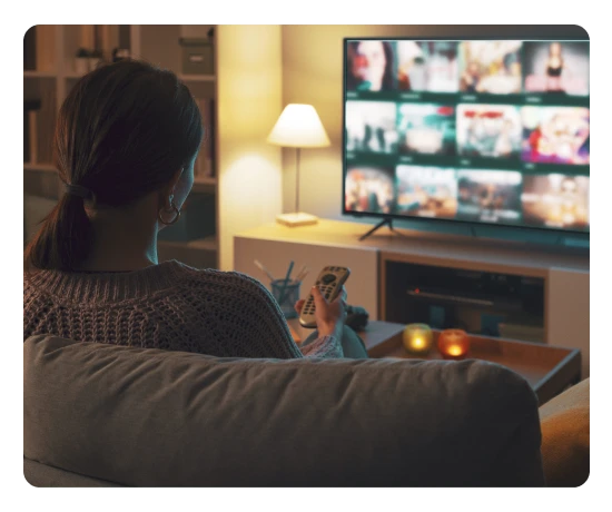 Pessoa sentada no sofá a ver televisão numa sala com luz ambiente