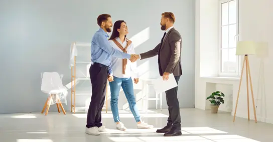 Casal a apertar a mão a um agente imobiliário numa sala vazia