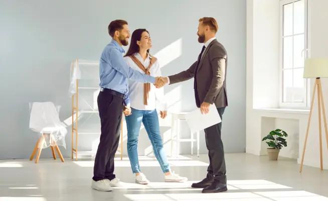 Casal a apertar a mão a um agente imobiliário numa sala vazia