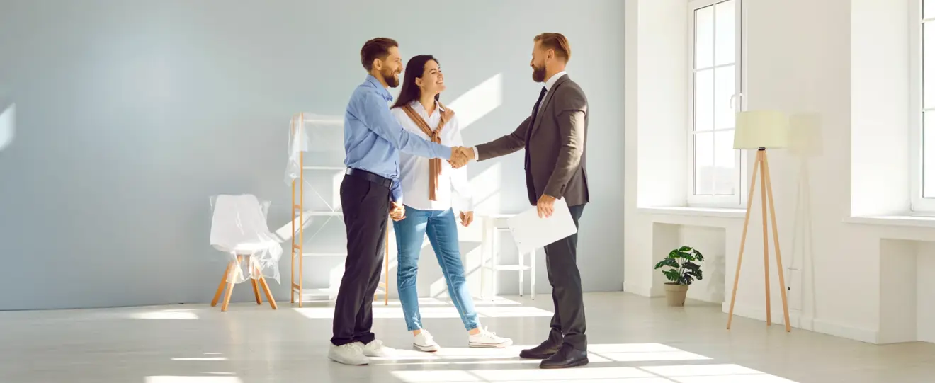 Casal a apertar a mão a um agente imobiliário numa sala vazia