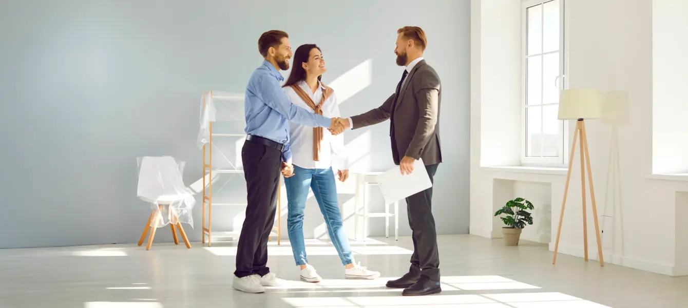 Casal a apertar a mão a um agente imobiliário numa sala vazia