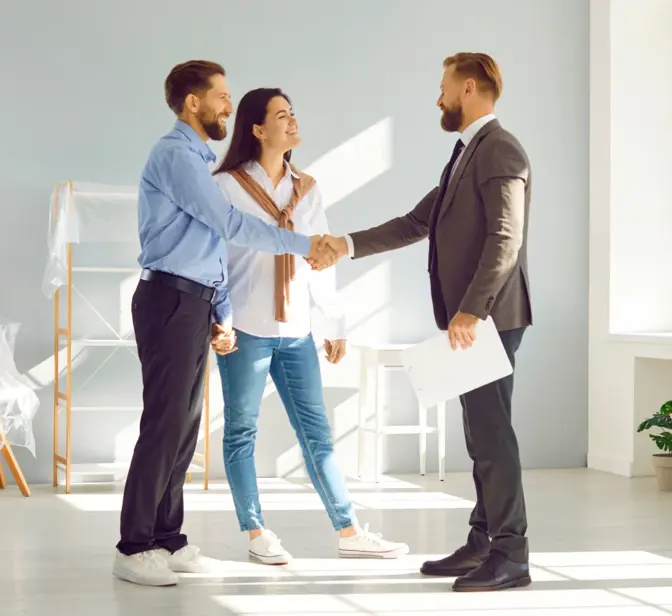 Casal a apertar a mão a um agente imobiliário numa sala vazia