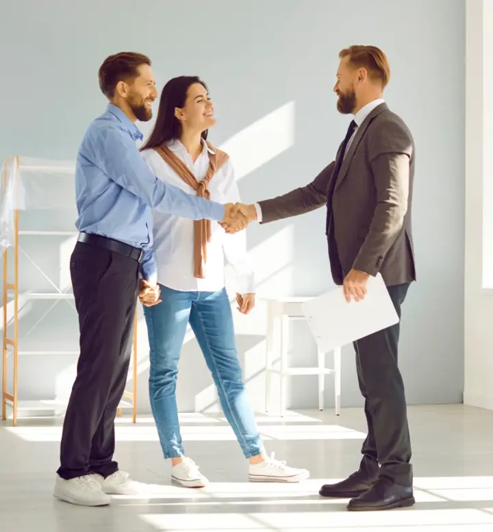 Casal a apertar a mão a um agente imobiliário numa sala vazia