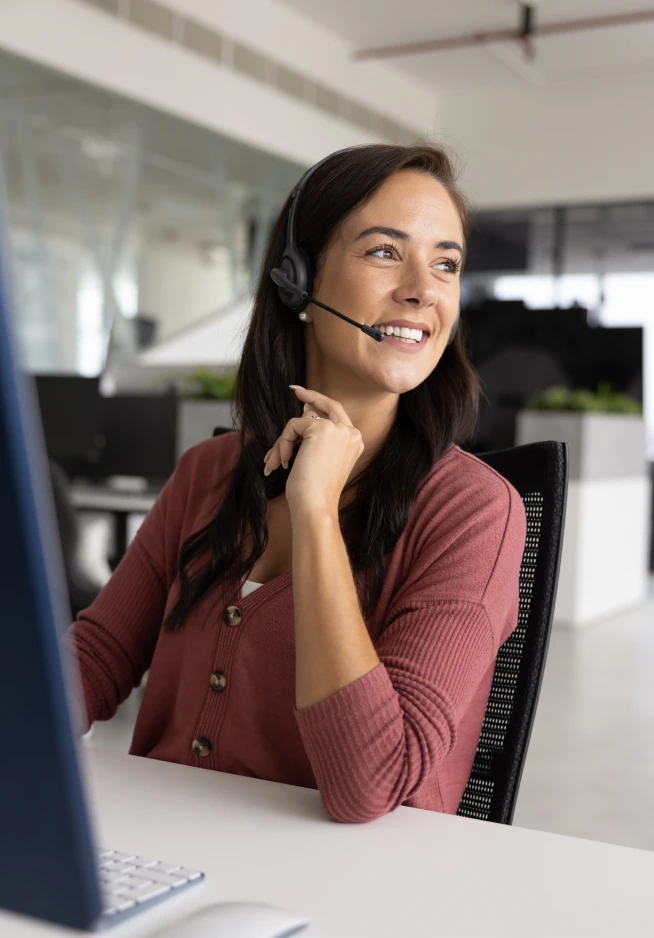 senhora sorridente num centro de contactos, com headset e computador