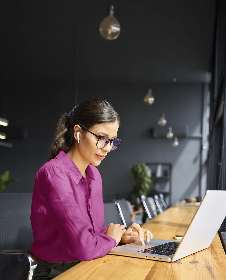 senhora sentada, com mesa de madeira corrida à frente, onde tem o seu computador