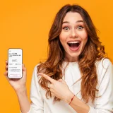 Senhora jovem a sorrir e com telemóvel na mão