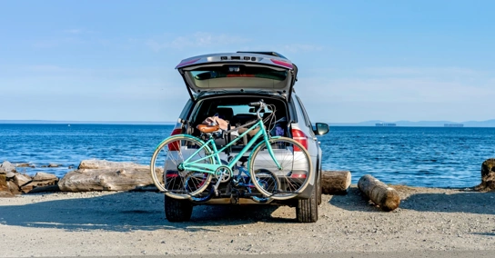 Carro com bicicleta no suporte estacionado numa praia de frente para o mar