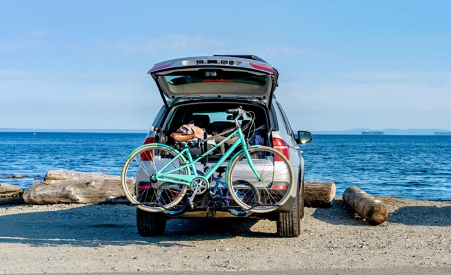 Carro com bicicleta no suporte estacionado numa praia de frente para o mar