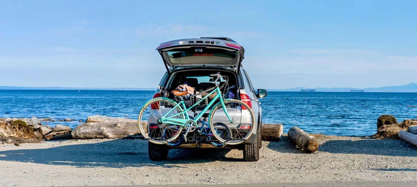 Carro com bicicleta no suporte estacionado numa praia de frente para o mar