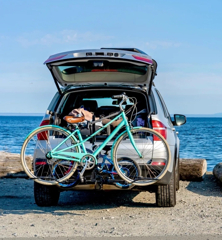 Carro com bicicleta no suporte estacionado numa praia de frente para o mar