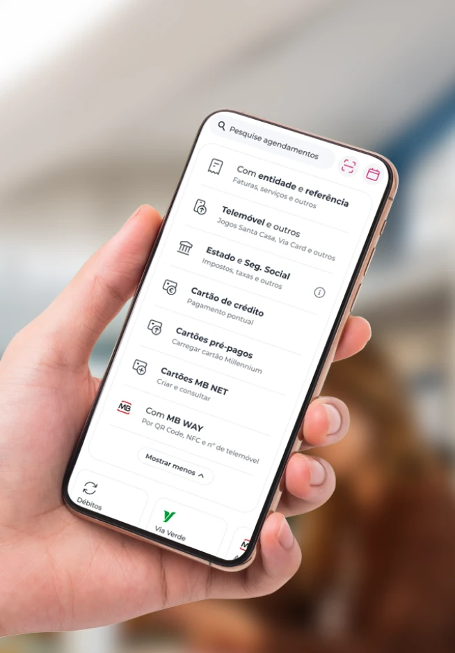 Mão a segurar num telemóvel, que no ecrã apresenta todos pagamentos possíveis de serem feitos através da App Millennium