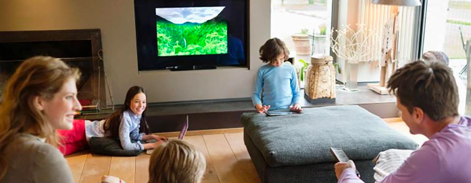 Família com pai, mãe e 3 filhos, na sala, com televisão, telemóvel e tablet