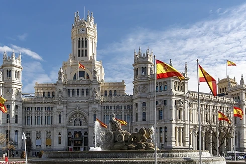 Cybele Palace and fountain in Madrid with Spanish flags under a blue sky