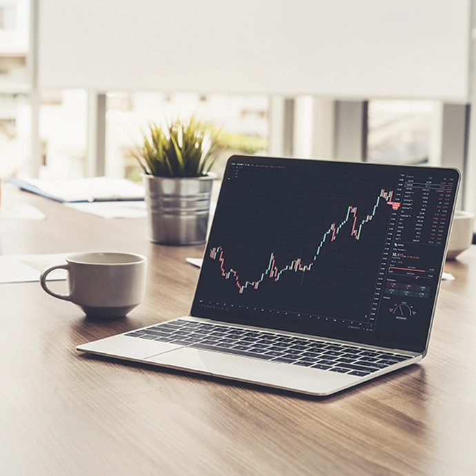 Computador portátil numa secretária a mostrar um gráfico de bolsa em subida