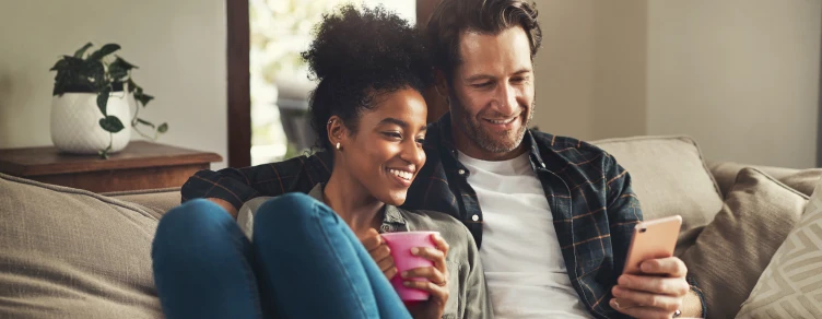 couple sitting on sofa, with coffee mugs, hugging and looking at his phone