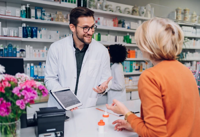 Jovem farmacêutico mostra um tablet a uma cliente sénior numa farmácia