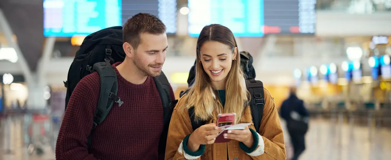 Casal de viajantes no aeroporto a olhar para um telemóvel