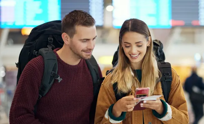 Casal de viajantes no aeroporto a olhar para um telemóvel
