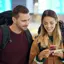 Casal de viajantes no aeroporto a olhar para um telemóvel