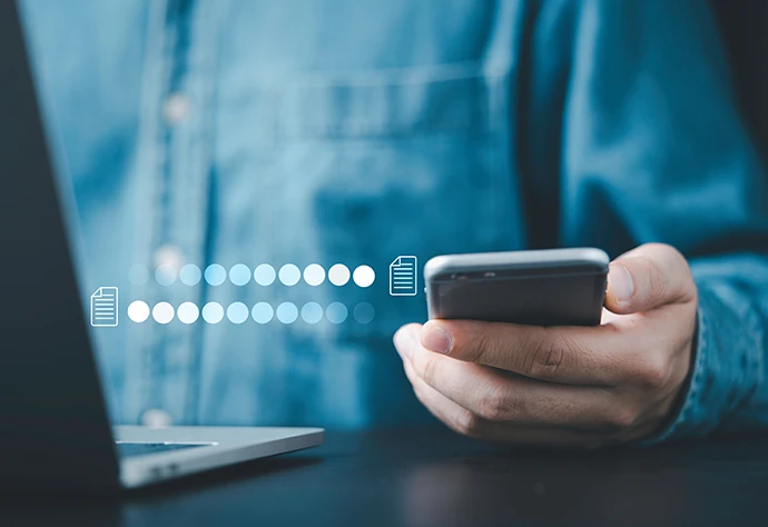 pormenor de mão a segurar telemóvel ao lado de computador