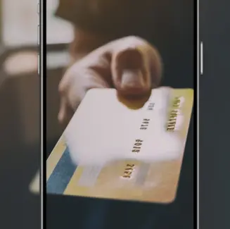 Mão a estender um cartão de crédito dourado, visível no ecrã de um telemóvel