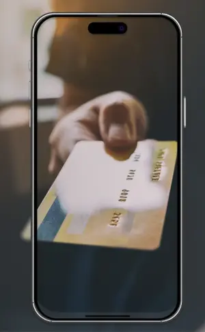 Mão a estender um cartão de crédito dourado, visível no ecrã de um telemóvel