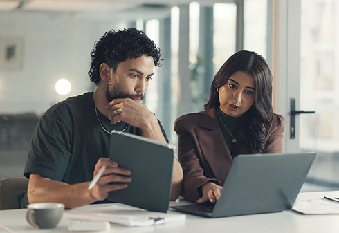 Um homem e uma mulher a analizar dados no ecrâ de um computador