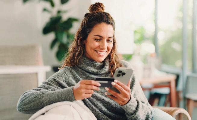 Mulher sorridente a fazer uma compra online no telemóvel com um cartão de crédito