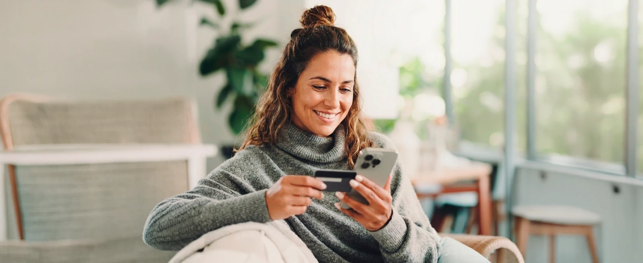 Mulher sorridente a fazer uma compra online no telemóvel com um cartão de crédito