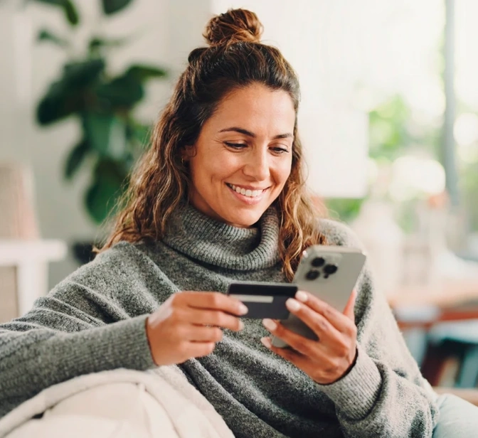 Mulher sorridente a fazer uma compra online no telemóvel com um cartão de crédito