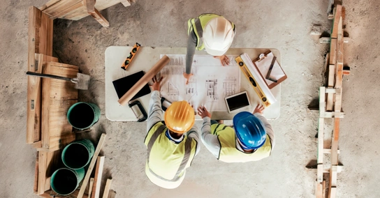 Três trabalhadores da construção a analisar plantas de uma obra, vistos de cima