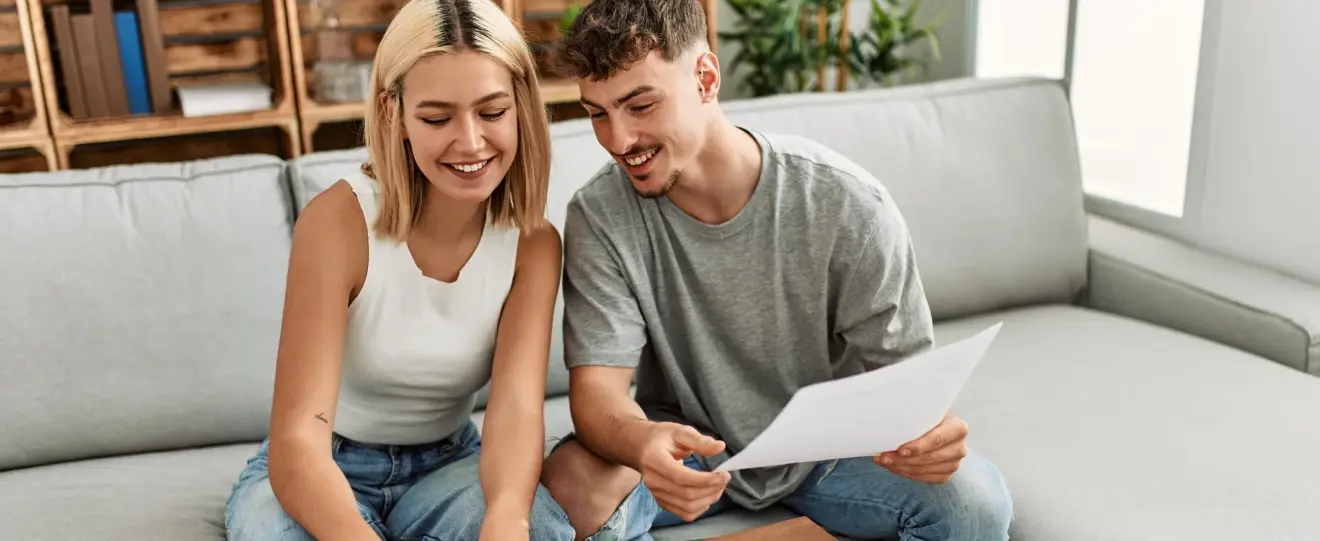 Casal sorridente no sofá a ver documentos e um portátil