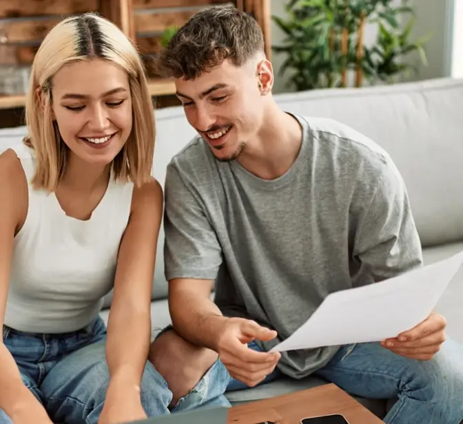 Casal sorridente no sofá a ver documentos e um portátil