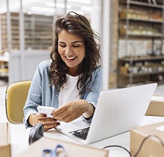 senhora sorridente numa secretária num armazém, com TPA na mão