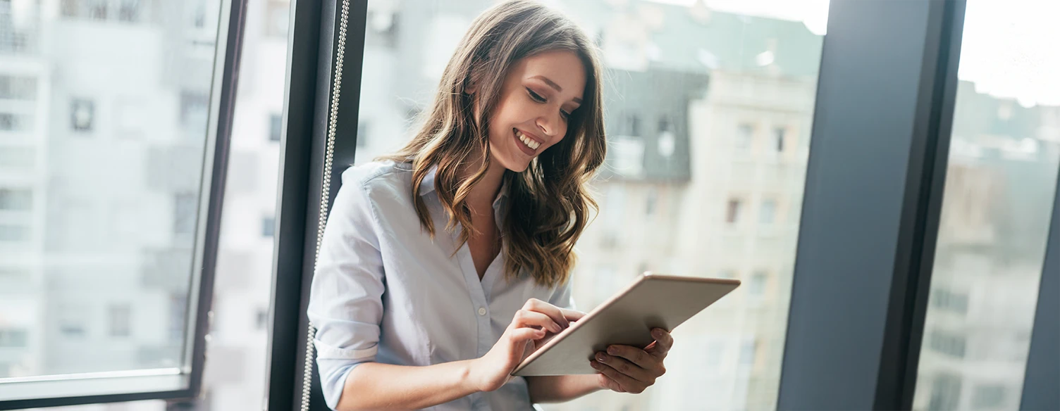 senhora sorridente à janela com tablet