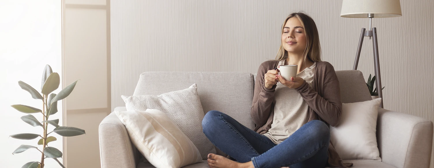 senhora sentada no sofá com pernas cruzadas e chávena na mão, com ar tranquilo