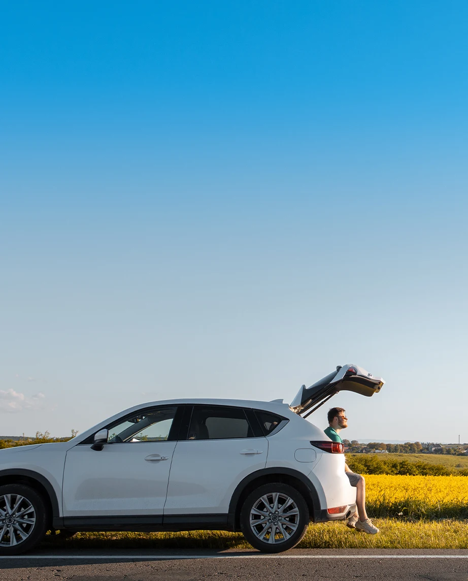  white car parked on the roadside, with the trunk open and a man sitting inside