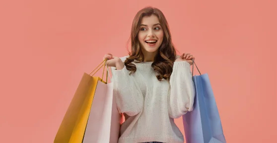 Rapariga com uma camisola de malha e calças de ganga a levantar 3 sacos de compras com as duas mãos