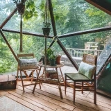 Interior de um domo geodésico com mobiliário rústico e vista para a floresta