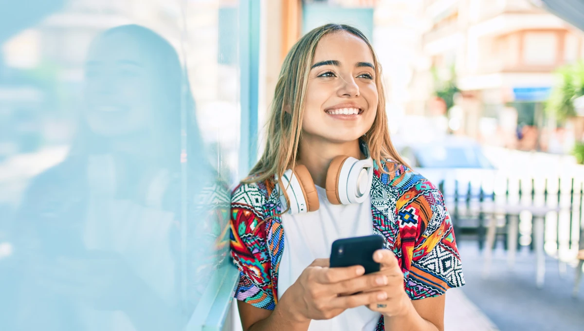 rapariga a sorrir com headphones e com telemóvel na mão