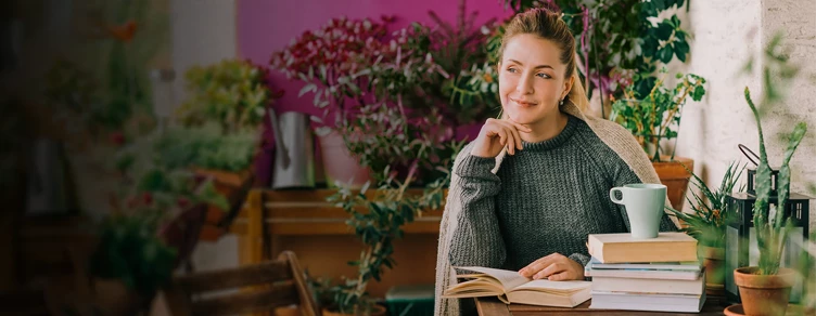 smiling lady, seated at a table with plants, books, and a cup of tea