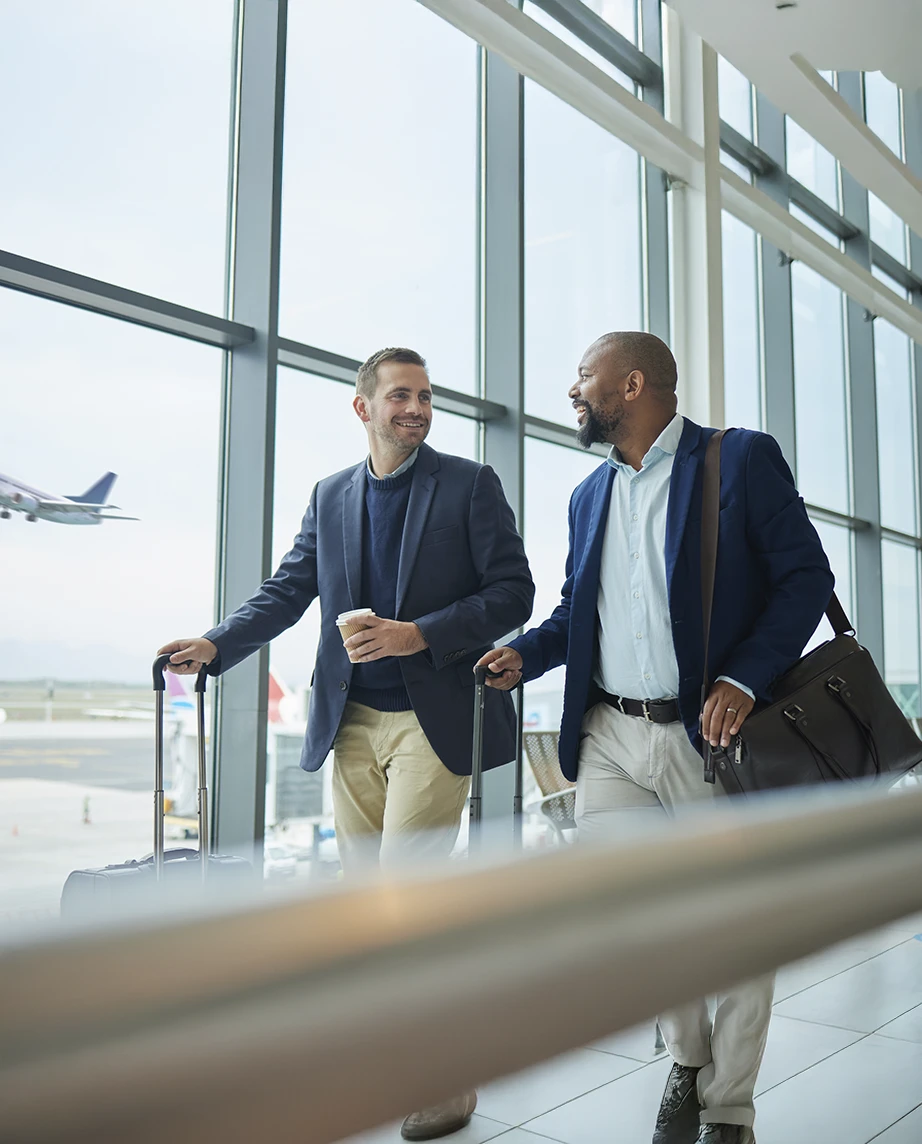 Dois homens no Aeroporto, a caminhar lado a lado a conversar, transportando a suas bagagens
