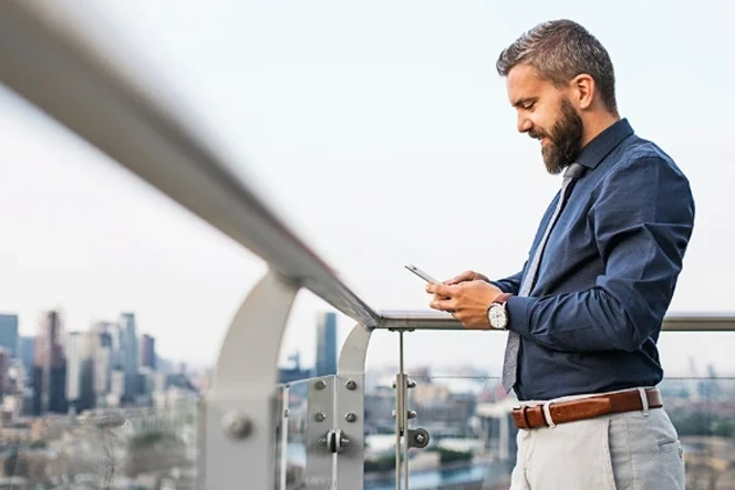 Homem de negócios a usar o telemóvel numa varanda com vista para a cidade
