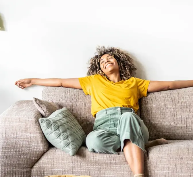 Mulher sorridente a relaxar no sofá com os braços estendidos