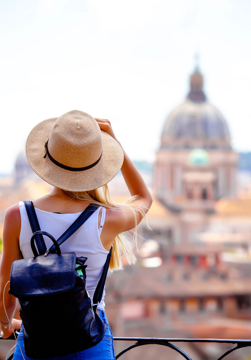 Girl with her back turned, wearing a hat and a backpack, looking at a monument in the distance