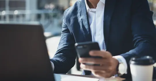 Homem de fato a usar telemóvel com portátil e café na mesa