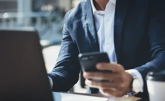 Homem de fato a usar telemóvel com portátil e café na mesa