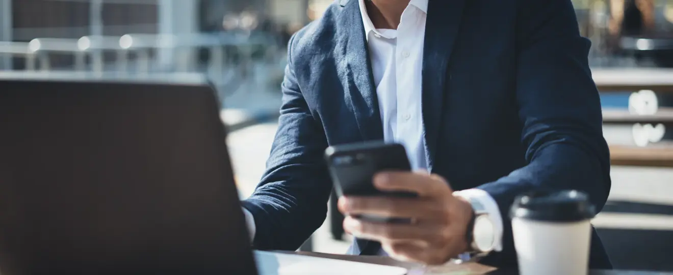 Homem de fato a usar telemóvel com portátil e café na mesa